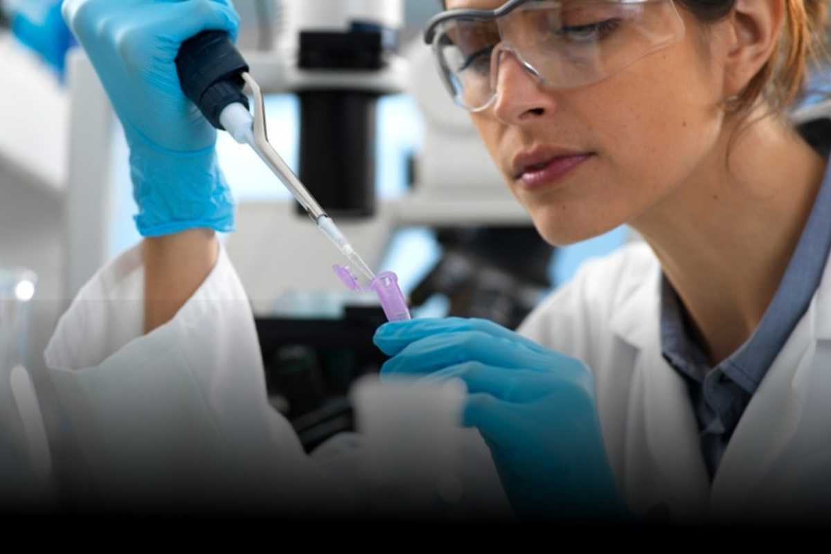 Duas pessoas de jaleco e óculos de proteção manipulando uma pipeta em laboratório