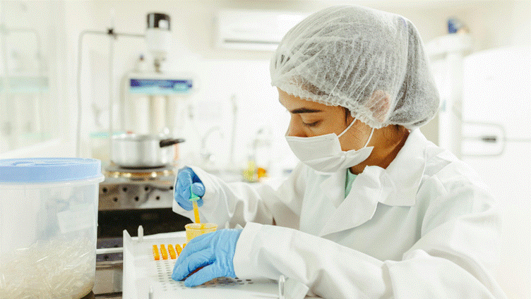 Profissional de touca e máscara trabalhando com amostras numa bancada de laboratório