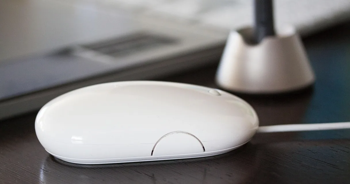 Mouse de computador branco sobre uma mesa de trabalho, ilustrando a mão que dói depois de digitar